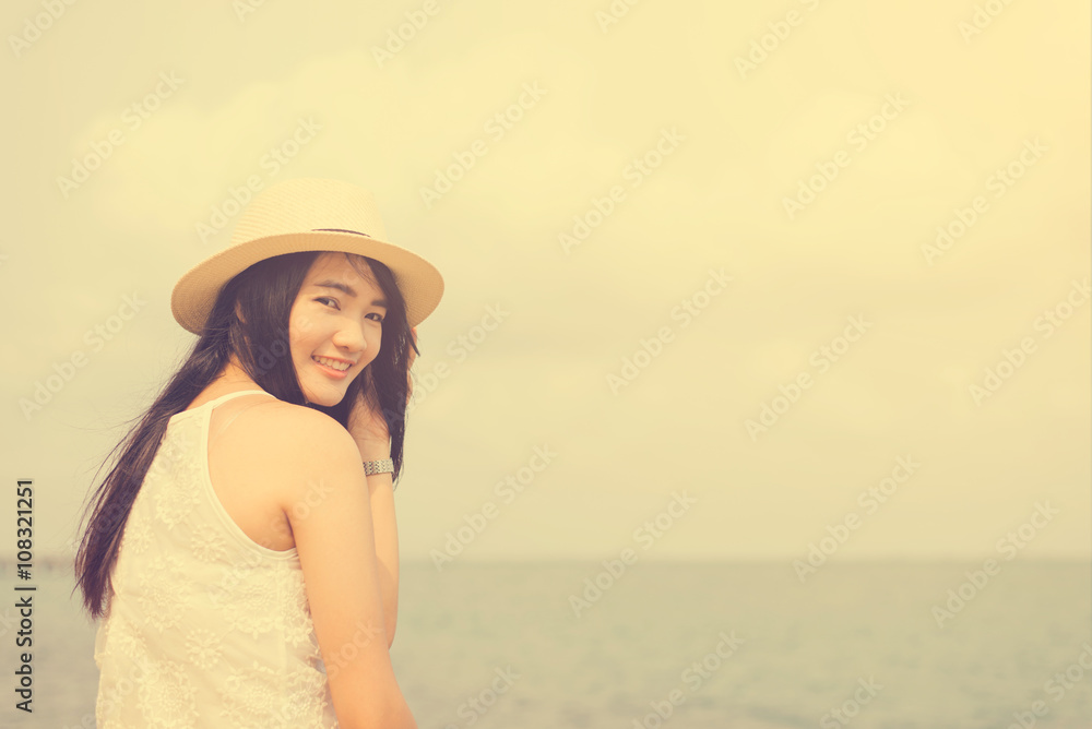 Outdoor summer portrait of young pretty woman looking to the ocean at tropical beach, enjoy her freedom and fresh air, wearing stylish hat and clothes, Vintage filtered image.