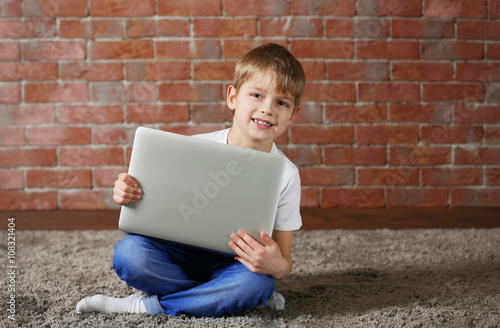 Little boy with laptop on fur carpet against brick wall background
