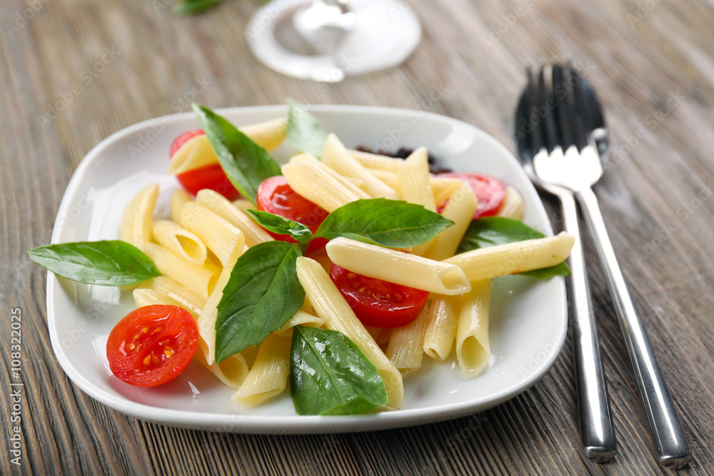 Plate of pasta with cherry tomatoes and basil leaves on table closeup Plate of pasta with cherry tomatoes and basil leaves on table closeup