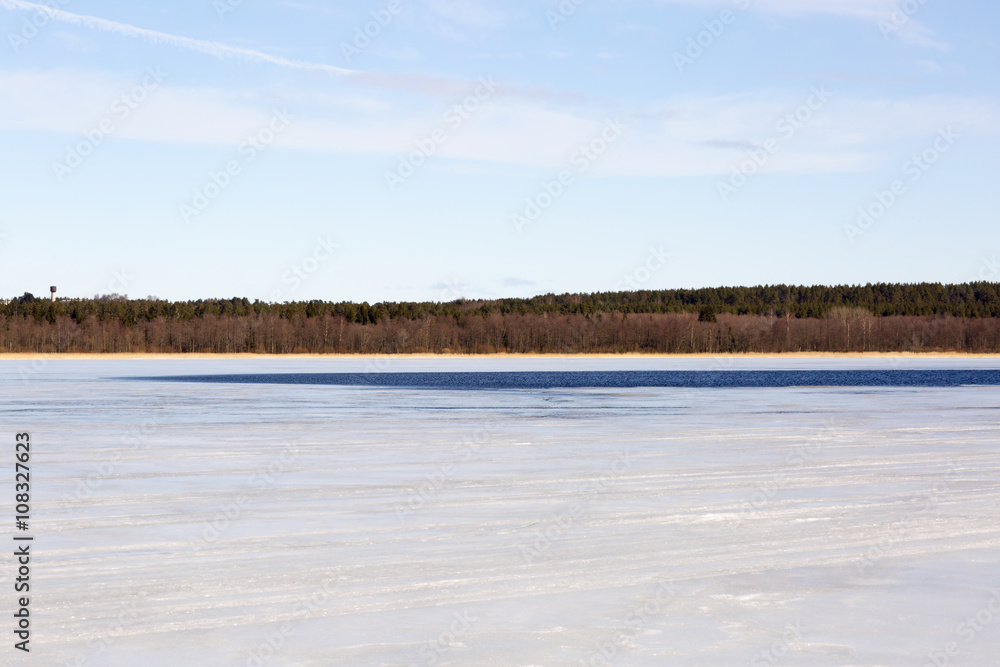 Frozen lake and cloudy sky. The lake is covered with ice in the woods. 