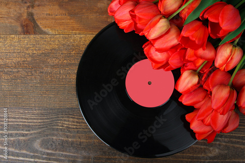 old black plates for the gramophone near the pile of red tulips on wooden background