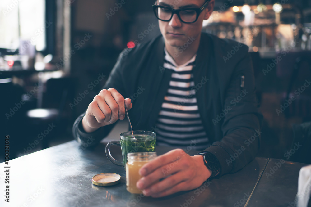 Hipster man with retro glasses putting honey in fresh mint tea Hipster man with retro glasses putting honey in fresh mint tea