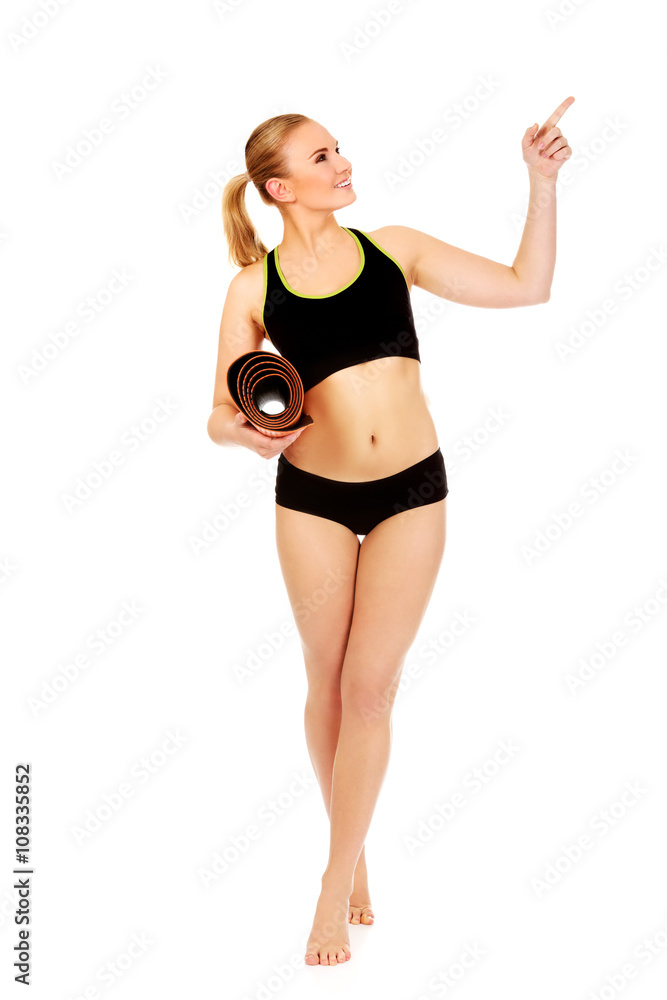 Young athletic woman holding mat and pointing for something Young athletic woman holding mat and pointing for something