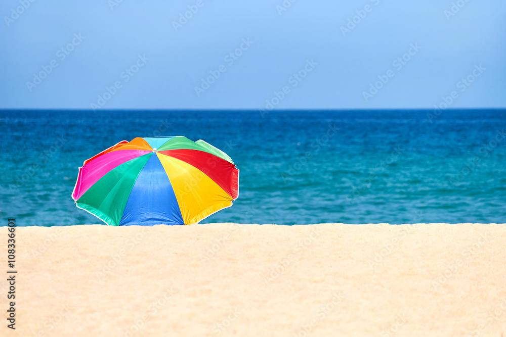 Разноцветный зонтик от солнца на пустынном песчаном пляже.