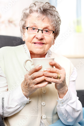 Starsza pani pije napar z ziół. Starsza kobieta odpoczywa na fotelu z kubkiem naparu z ziół