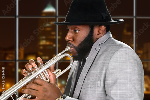 Guy in hat plays trumpet. Afro trumpeter on night background. Young ska musician on tour. Music of big city.