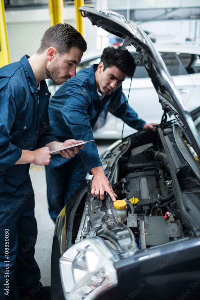 Mechanics examining car engine using digital tablet Mechanics examining car engine using digital tablet