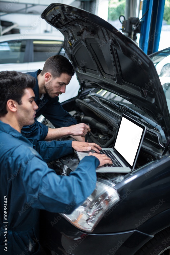 Mechanics examining car engine using laptop Mechanics examining car engine using laptop