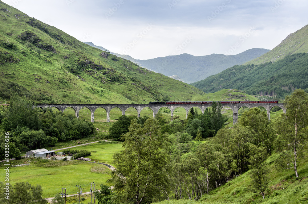 Glenfinnan, Scotland - - July 11, 2015: Viaduct with train and mountains in the background. The spot became famous through movies such as Harry Potter.