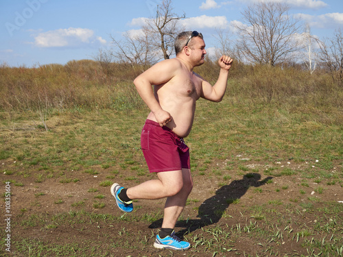 Fototapeta Naklejka Na Ścianę i Meble -  Fat man running outdoors on nature.