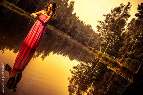 Unique outdoor portrait of violist playing on her violin during calm summer sunrise in lake near to Rybnik Poland