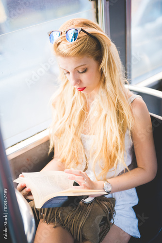 Young beautiful caucasian blonde woman sitting on a bus reading a book - student, commuter, transport concept photo
