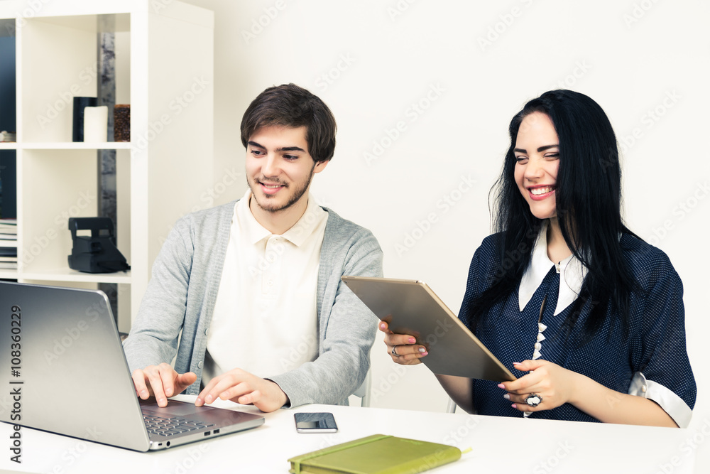 Two young people working together with laptop and tablet  while sitting at minimalistic white office