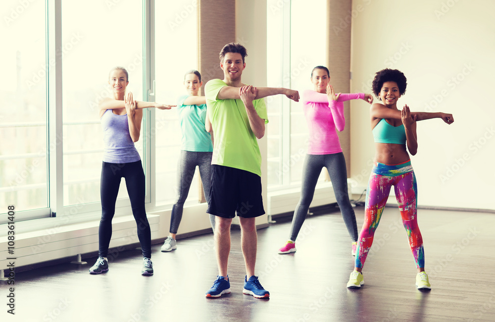 Fototapeta premium group of smiling people stretching in gym