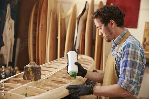 Carpenter gluing bespoke wooden surfboard in workshop photo