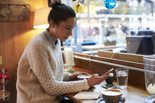 Young Woman Sitting In Coffee Shop Reading Text Message