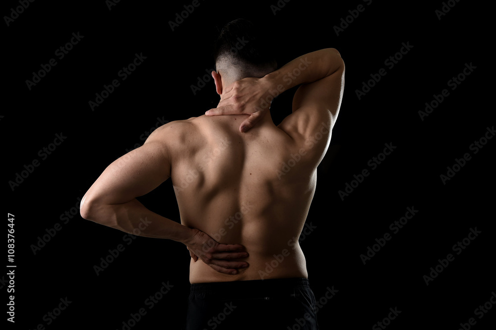 back view of young man with muscular body holding his neck and low back suffering spinal pain