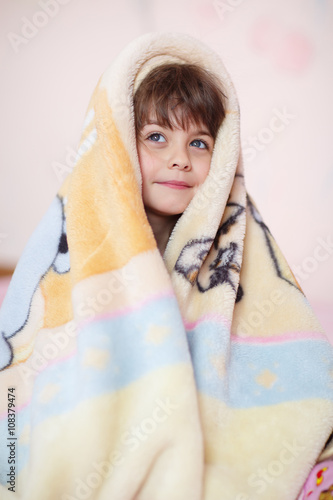 beautiful little sweet girl hiding under a warm plush blanket. The child slyly peeking out from under the blankets