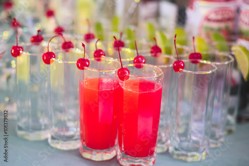 Beautiful row line of different colored alcohol cocktails with mint on a tropical Hawaiian hawaii style party, martini, vodka,and others on decorated catering bouquet table on open air beach event