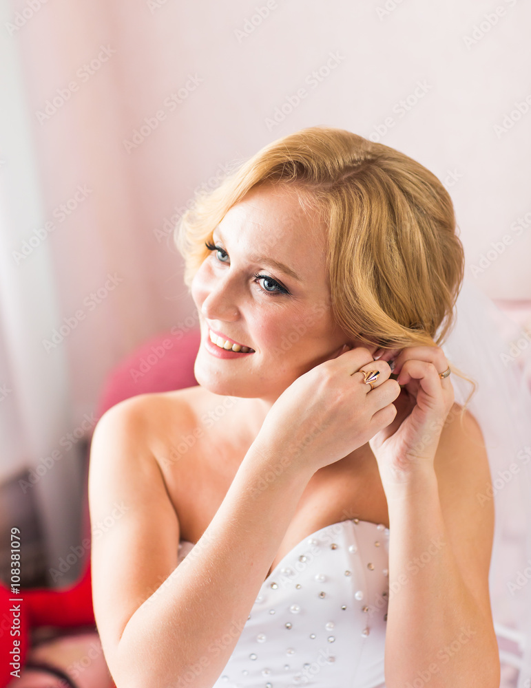 Naklejka premium Beautiful elegant bride putting on earrings closeup, wedding preparation.