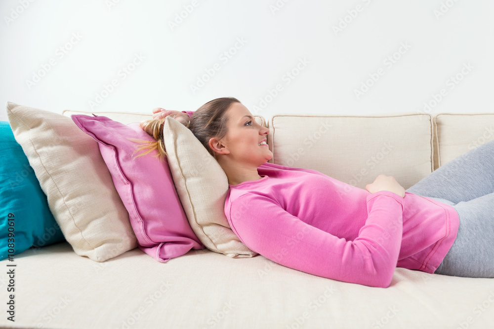 Beautiful young woman relaxing at home while lying on bunch of pillows on a sofa in a living room Beautiful young woman relaxing at home while lying on bunch of pillows on a sofa in a living room