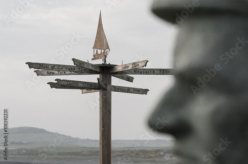 The head of a sculpture appears to be contemplating which direction to take as a sign post in the background offers different destinations