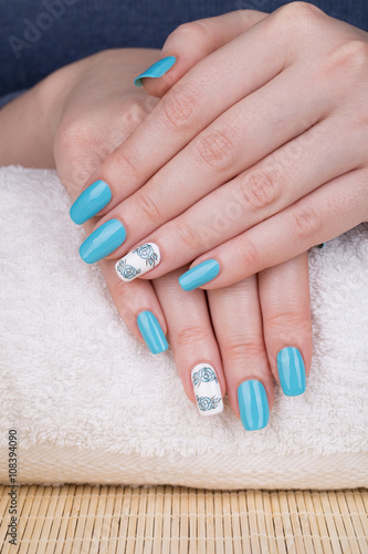 Manicure - Beauty treatment photo of nice manicured woman fingernails with blue polish and flower design on accent nail.