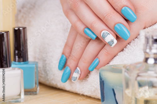 Manicure - Beauty treatment photo of nice manicured woman fingernails with blue polish and flower design on accent nail.