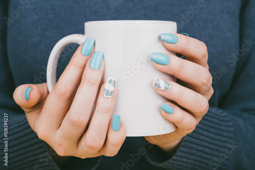 Manicure - Beauty treatment photo of nice manicured woman fingernails holding a cup. Nice blue polish and flower design on accent nail.