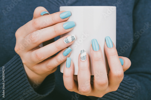 Manicure - Beauty treatment photo of nice manicured woman fingernails holding a cup. Nice blue polish and flower design on accent nail.