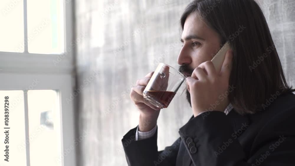 Young man wearing suit talking on a mobile phone in the morning at a window with copy space, Young man wearing suit talking on a mobile phone in the morning at a window with copy space,