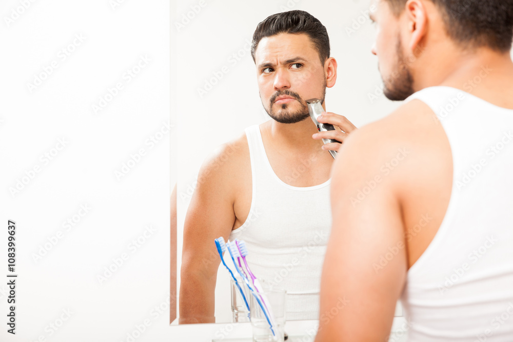 Fototapeta premium Young man trimming his beard in the bathroom