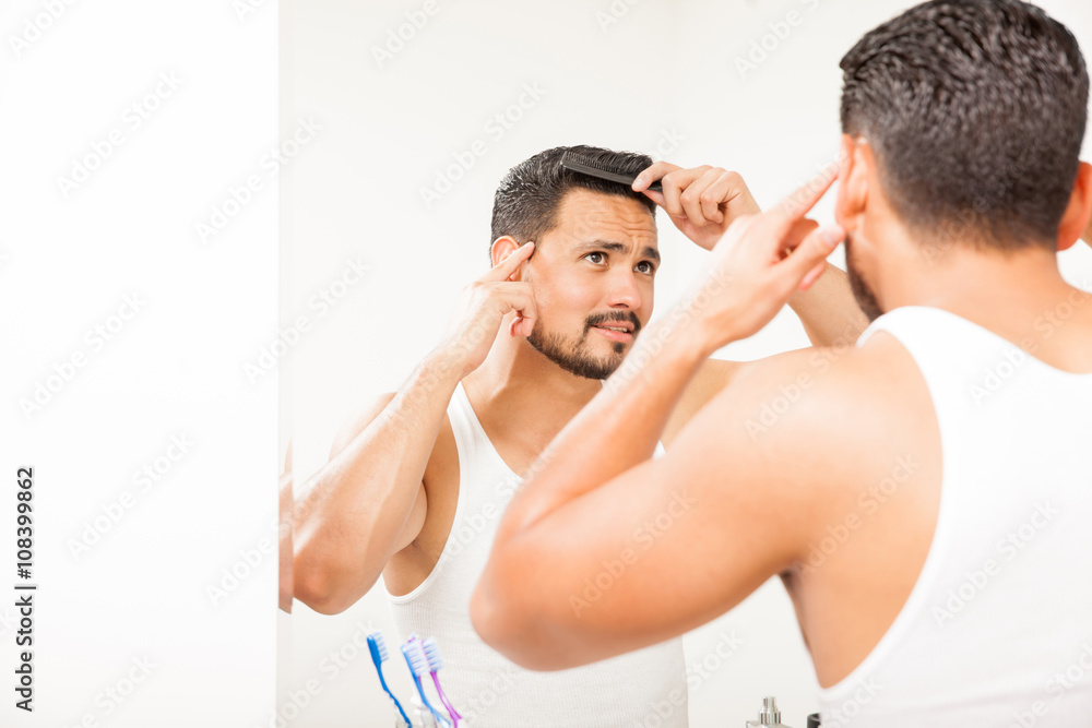 Fototapeta premium Attractive guy combing his hair in the bathroom