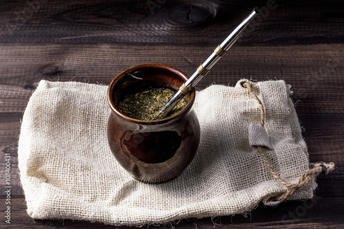 Yerba mate in ceramic matero with bombilla on linen bag on wooden table. photo