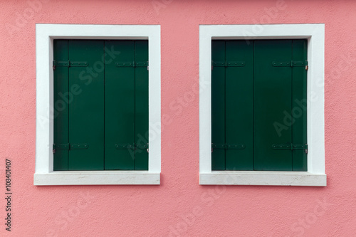 Two old windows with dark green shutters on light pink wall
