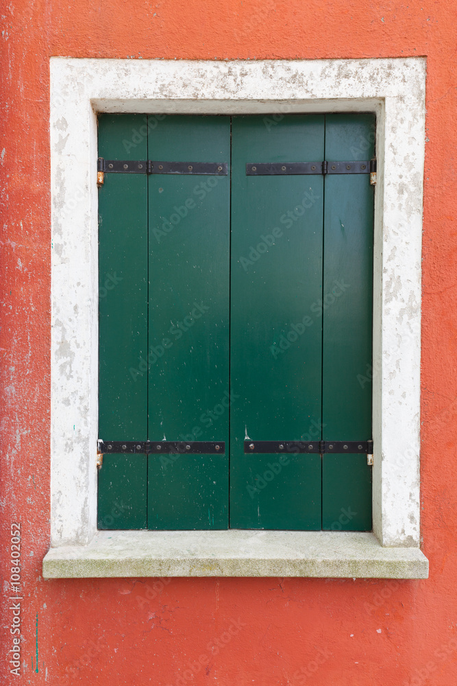 Old window with green shutters on red wall