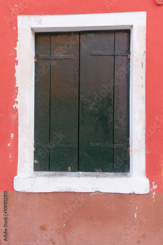 Old window with dark green shutters on red wall