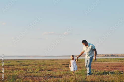 Папа гуляет со своей маленькой дочерью за руку на широком летнем открытом пространстве