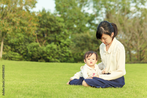 公園の芝に座り赤ちゃんと遊ぶお母さん © Qiteng T