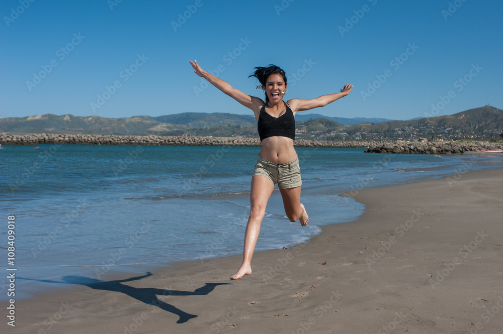 Young and energetic Latina beauty leaping across ocean shoreline. Young and energetic Latina beauty leaping across ocean shoreline.