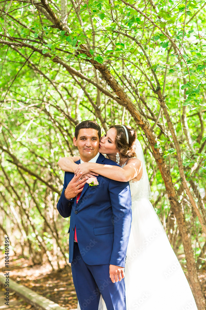 wedding couple hugging, the bride holding a bouquet of flowers, groom embracing her outdoors wedding couple hugging, the bride holding a bouquet of flowers, groom embracing her outdoors