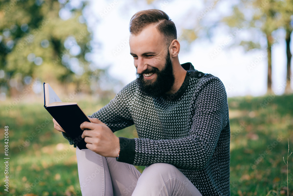 Fototapeta premium Bearded man hipster student reading a book and relax in park, exams