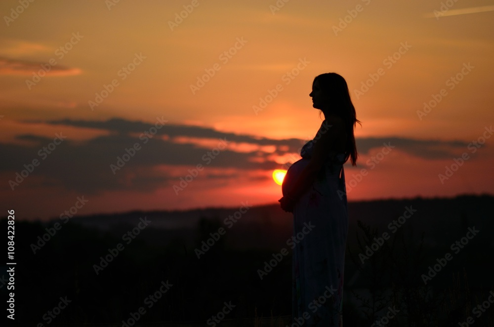 the pregnant girl with a hat in the field of wheat on a sunset