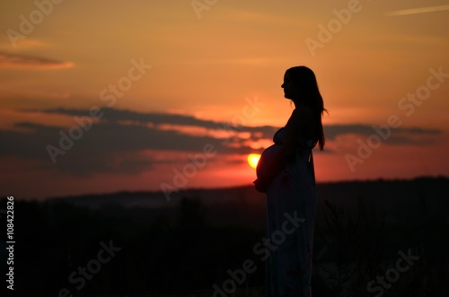 the pregnant girl with a hat in the field of wheat on a sunset