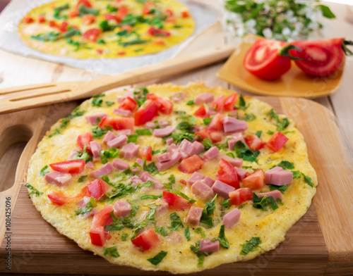 Omelette with vegetables on wooden background.