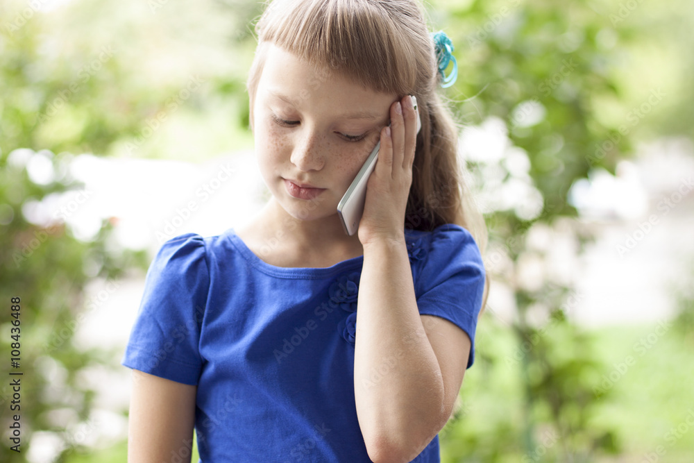 Little girl summer park talking on the phone, in a blue dress. Blonde Little girl summer park talking on the phone, in a blue dress. Blonde