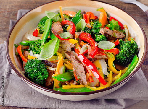 Beef stir fry with vegetables on wooden table.