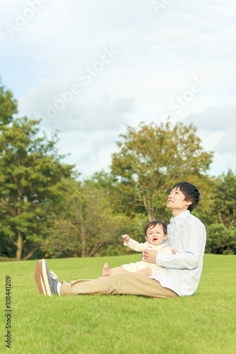 公園の芝生に座り、女の子の赤ちゃんと遊ぶお父さん