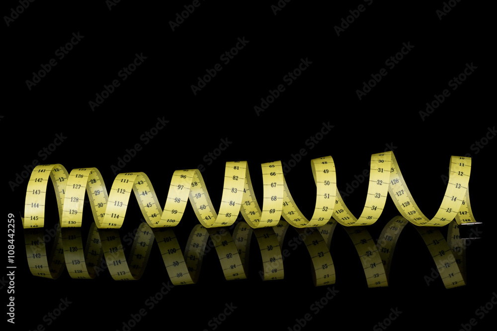 Fototapeta premium Yellow tape measure background - coiled on black, long.