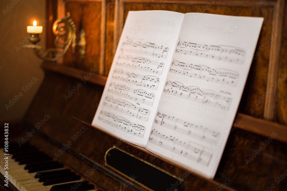 Fototapeta premium Opened Music Book on Beautiful Old Piano with Burning Candle